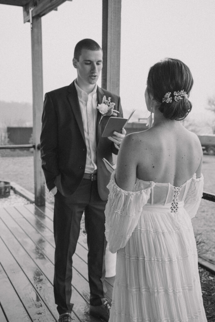 A couple's elopement ceremony on a porch in Pennsylvania. The groom is reading his vows from a book.