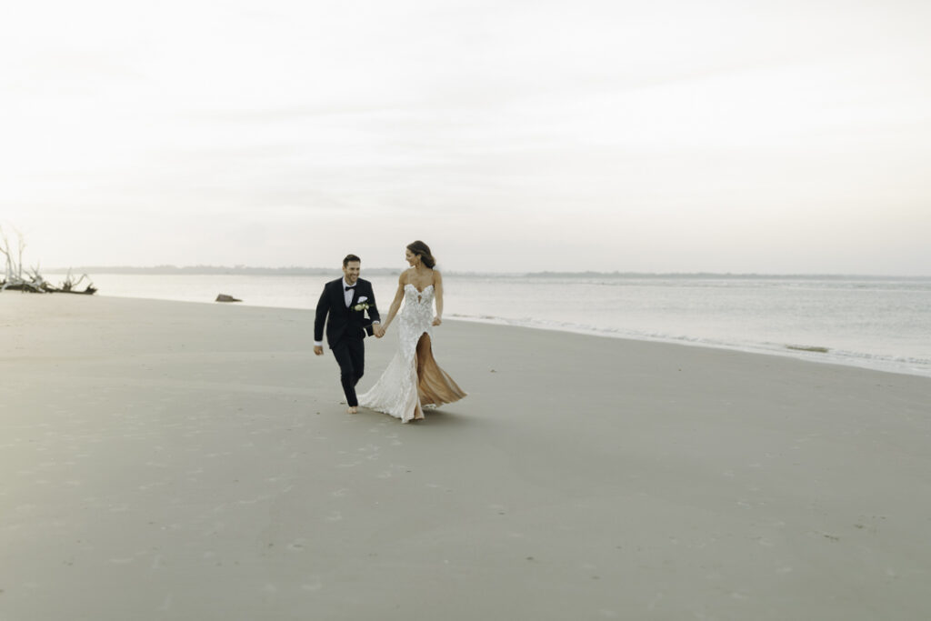 A couple on a beach in South Carolina, one of the best places to elope on the east coast. They're in their elopement attire, holding hands and running in the sand.